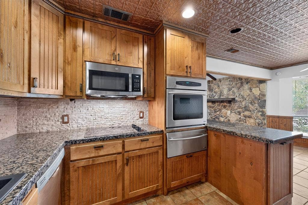 Kitchen featuring natural wood cabinetry, granite countertops, a built-in stainless steel microwave, and a double oven
