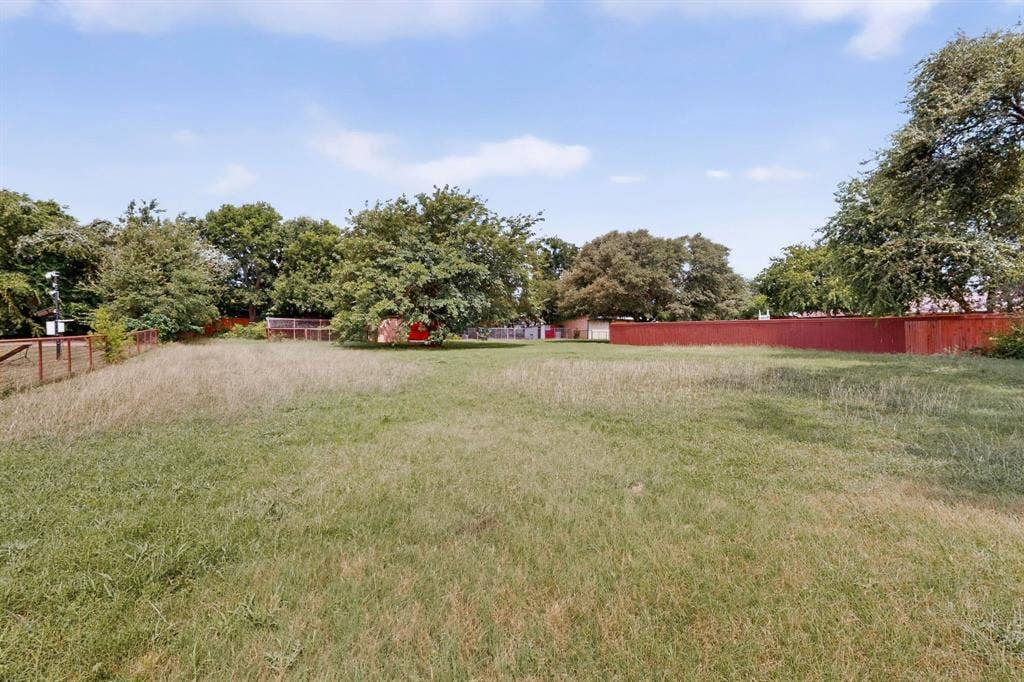 Expansive lot featuring a perimeter fence, mature trees, and a clear blue sky overhead