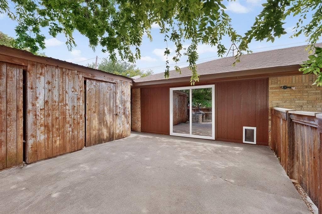 Concrete patio area featuring a shed with sliding wooden doors, a solid brown exterior wall, and a sliding glass door