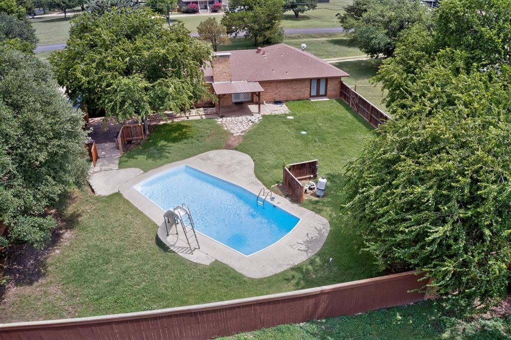 Expansive backyard featuring a large swimming pool with concrete surround, manicured lawn, and mature trees providing natural privacy