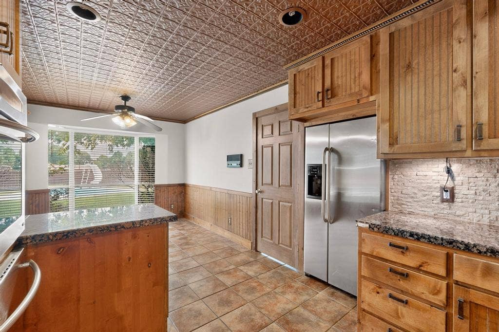 Kitchen featuring a tin-tile ceiling, wood-finish cabinetry, granite countertops, tile flooring, and a stainless steel side-by-side refrigerator