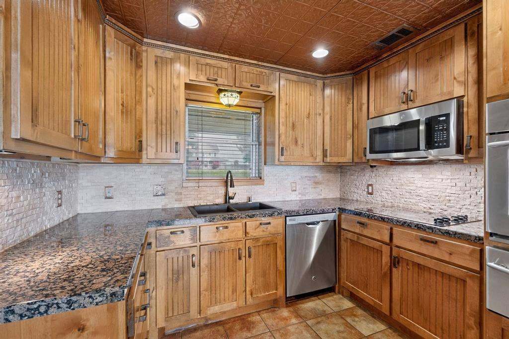 Kitchen featuring wood-finish cabinetry, granite countertops, tile backsplash, and a recessed sink with a gooseneck faucet