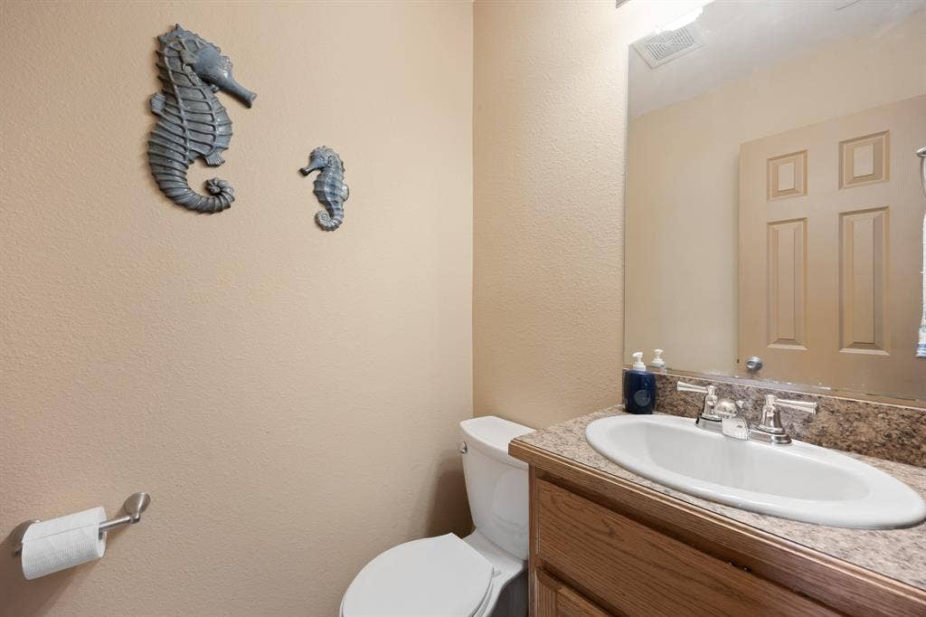 Powder room featuring a wood-finish vanity with an integrated sink, patterned countertop, and a large wall-mounted mirror
