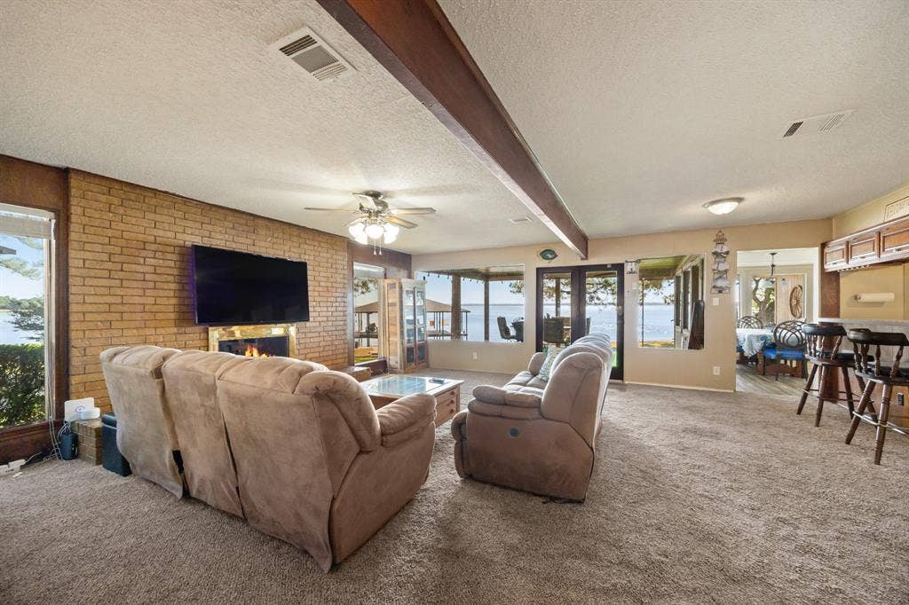 Living space featuring a brick-clad fireplace, wood beams, and a ceiling fan