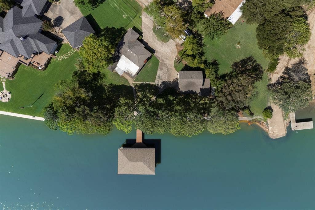 Waterfront property featuring a private boat dock with a covered slip, extensive green lawn, mature trees, and a concrete boat ramp