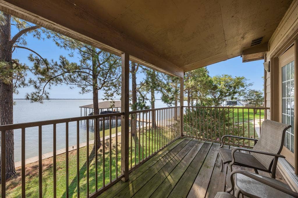 3B/3.5B Guest house with covered wood-deck balcony overlooking a body of water, featuring a metal railing, mature trees, and a boat dock
