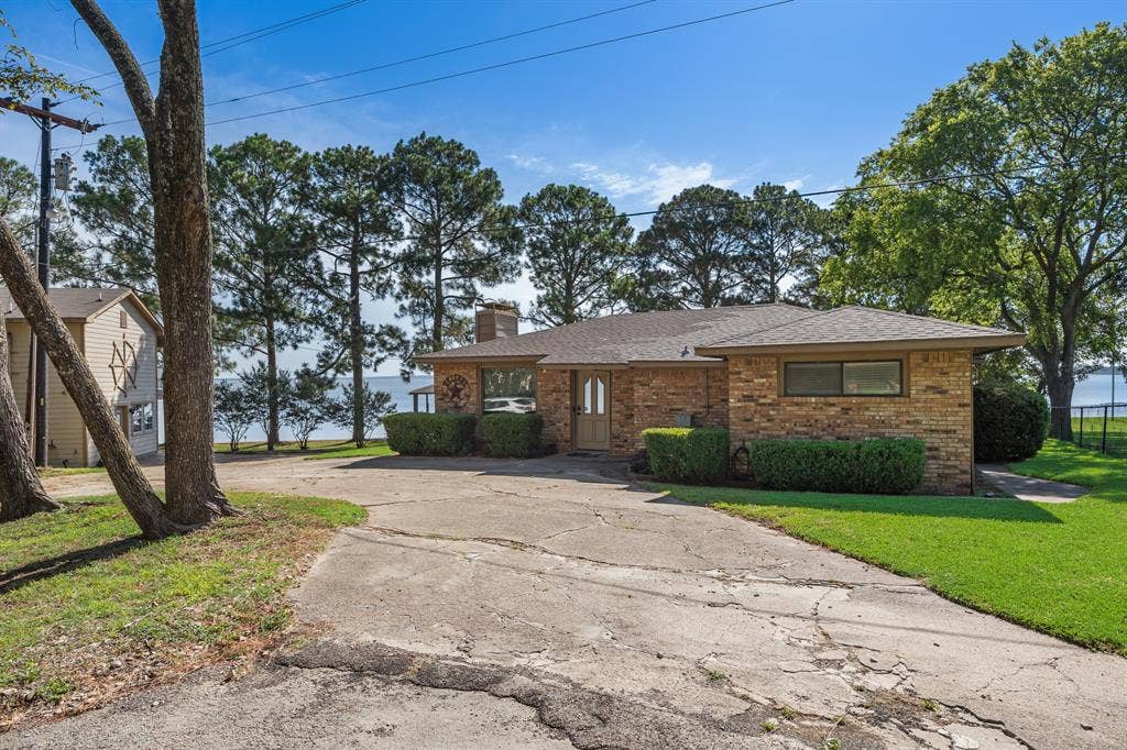 Brick exterior featuring a visible water body, mature trees, and a concrete driveway