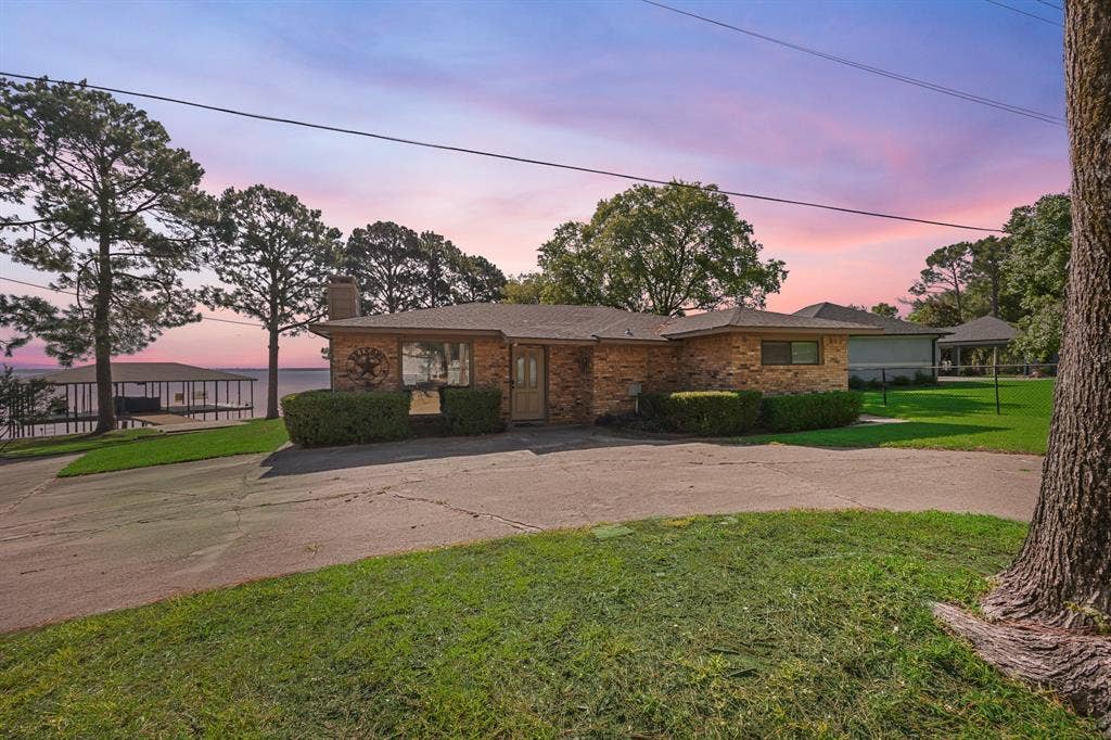 Brick exterior residence with a private driveway, mature trees, a manicured lawn, and water frontage featuring a private dock structure