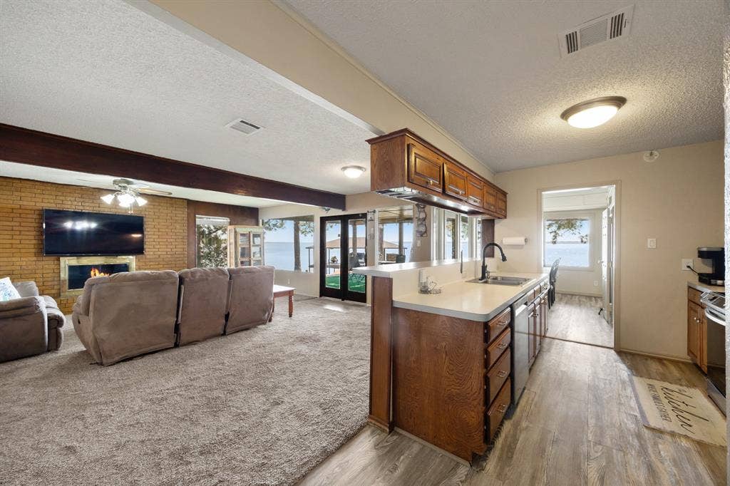 Open-concept living space with a brick fireplace, wood-finish flooring, and a kitchen featuring wood cabinetry, white countertops, and stainless steel appliances