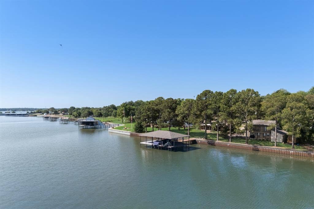 Waterfront property featuring a private boat dock, mature trees, and a spacious green lawn