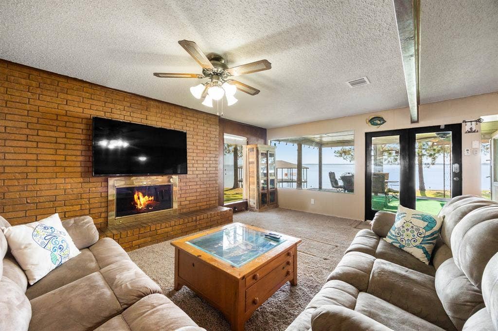 Living area featuring a brick fireplace, a ceiling fan, and large windows with water frontage
