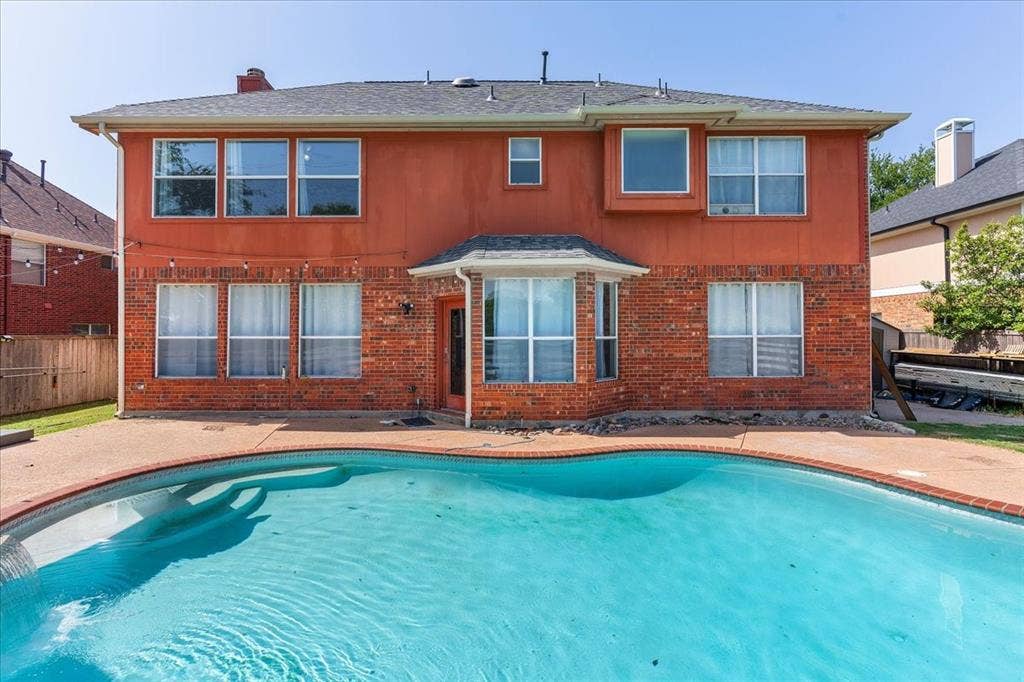 1013 Larkspur Drive, Allen, TX 75002 Curved swimming pool with concrete decking surrounds a two-story brick and stucco exterior