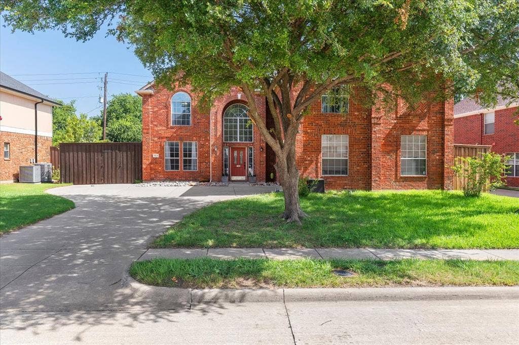 1013 Larkspur Drive, Allen, TX 75002 Traditional brick exterior featuring an arched entryway with a red door, multiple large windows, a mature front yard tree, and a concrete driveway