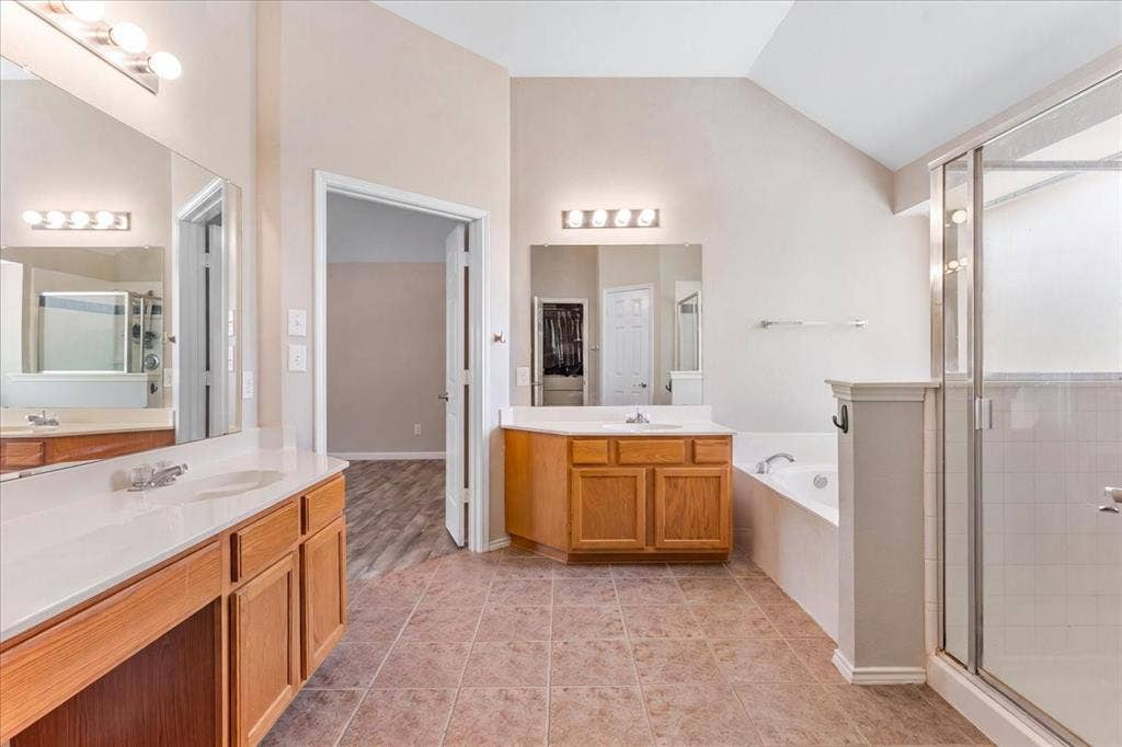 1013 Larkspur Drive, Allen, TX 75002 Spacious bathroom featuring twin vanities with integrated sinks and wood cabinetry, a tiled shower with a glass enclosure, an integrated soaking tub, and vaulted ceilings