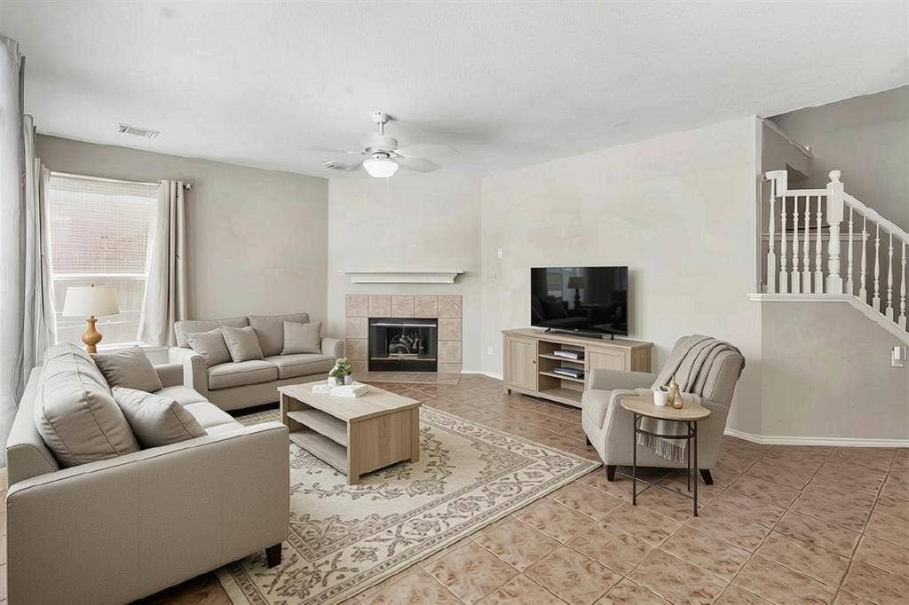 1013 Larkspur Drive, Allen, TX 75002 Living area featuring a tile-surround fireplace with a mantel, a ceiling fan with integrated lighting, and a white baluster staircase