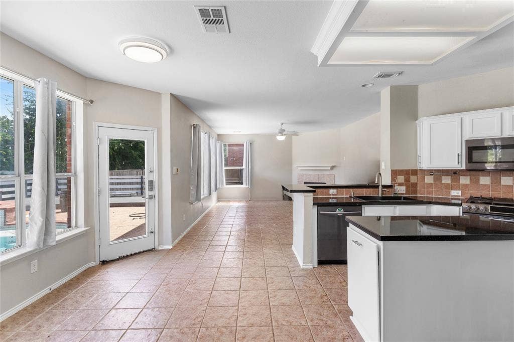 1013 Larkspur Drive, Allen, TX 75002 Spacious kitchen and dining area featuring white cabinetry, black granite countertops, stainless steel appliances, tile flooring, and abundant natural light from multiple windows and glass doors opening to an outdoor patio