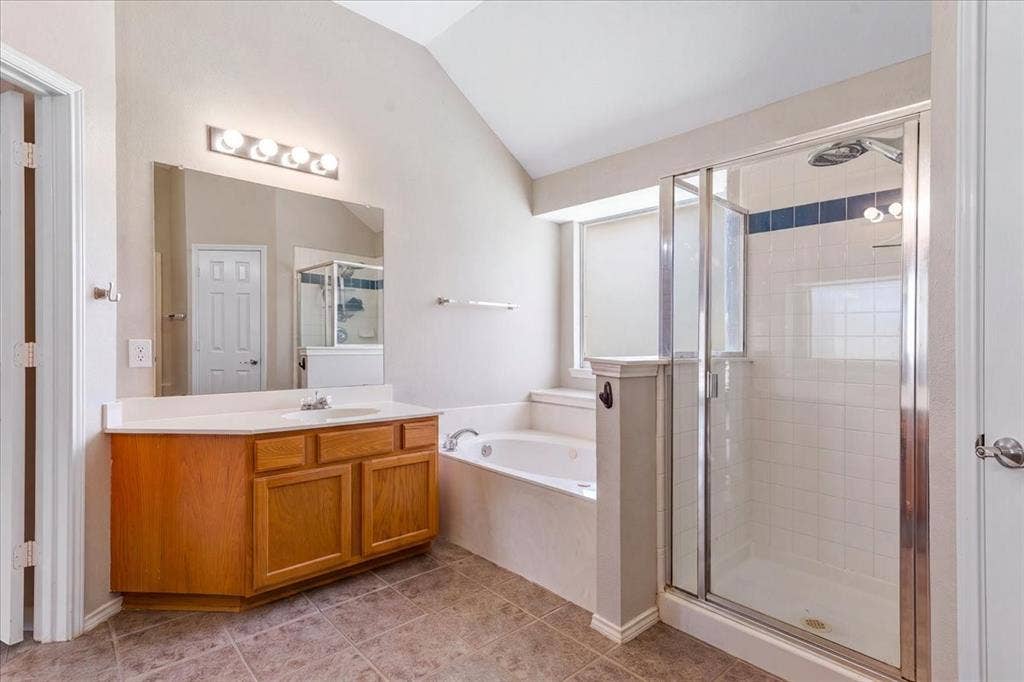 1013 Larkspur Drive, Allen, TX 75002 Bathroom featuring a wood-finish vanity with a single sink, a separate glass-enclosed shower, a built-in soaking tub, tile flooring, and a vaulted ceiling