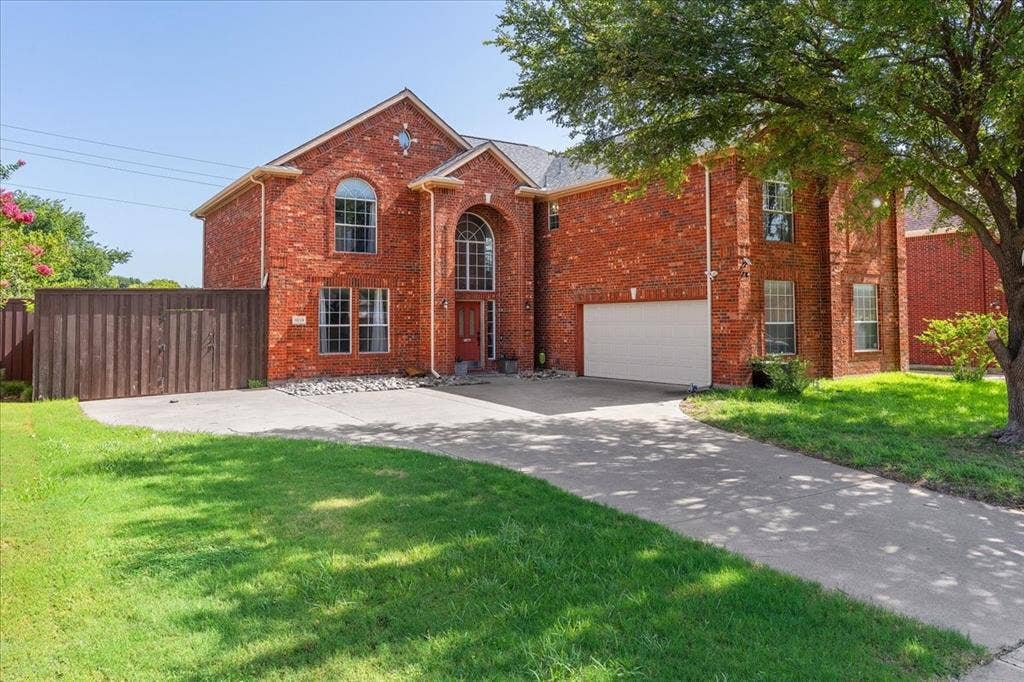 1013 Larkspur Drive, Allen, TX 75002 Red brick two-story residence featuring an arched entry, multiple window styles including arched and rectangular, an attached garage, and a concrete driveway