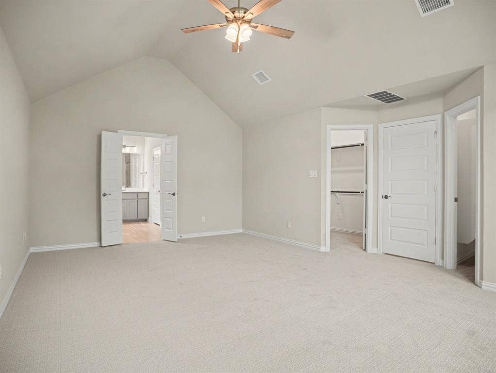 Spacious room featuring vaulted ceilings, light-toned carpeting, a ceiling fan with integrated lighting, and multiple access points including a double door entry to a bathroom and a closet with built-in shelving