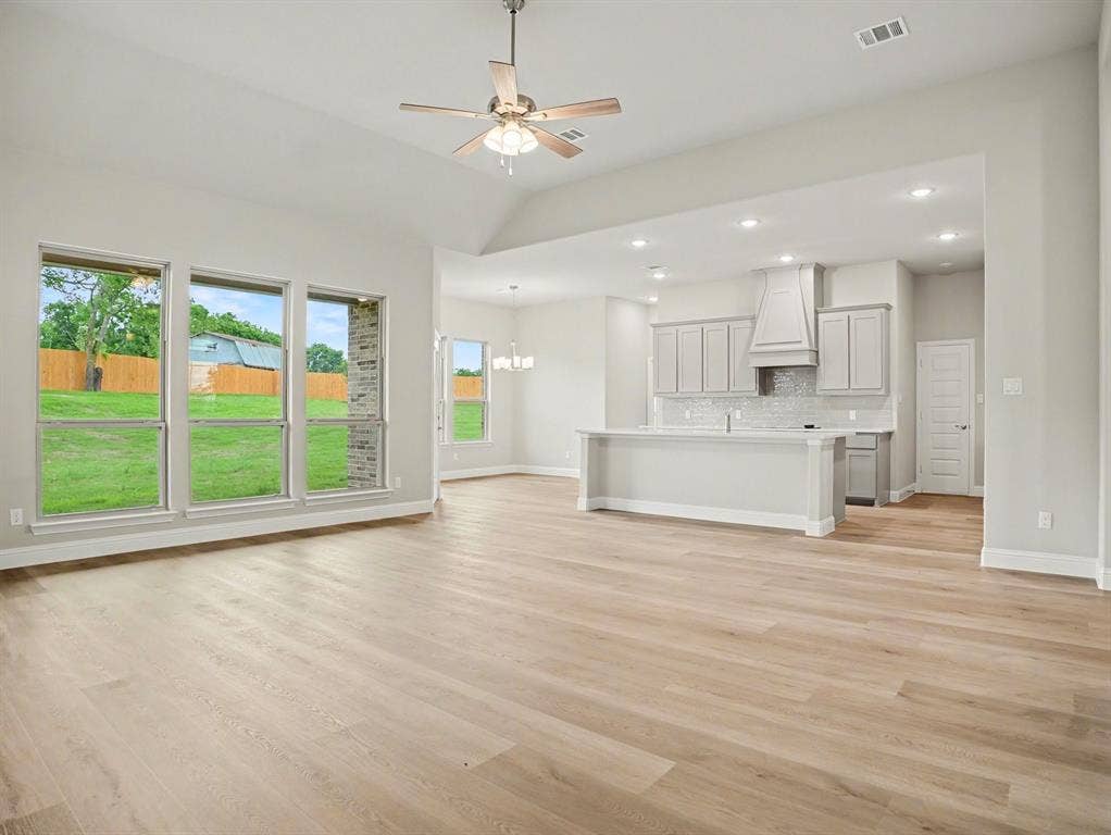 Open-concept living area featuring light wood-finish flooring, a vaulted ceiling with a ceiling fan, and multiple large windows