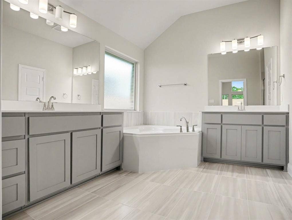 Spacious bathroom featuring a built-in corner soaking tub, dual vanities with light gray cabinetry and white countertops, and wood-finish tile flooring