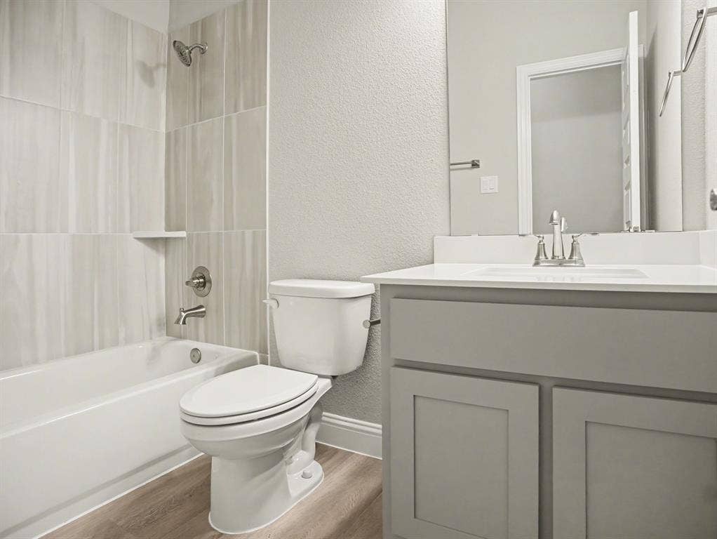 Bathroom featuring a white bathtub, a toilet, and a vanity with a white countertop and gray cabinetry