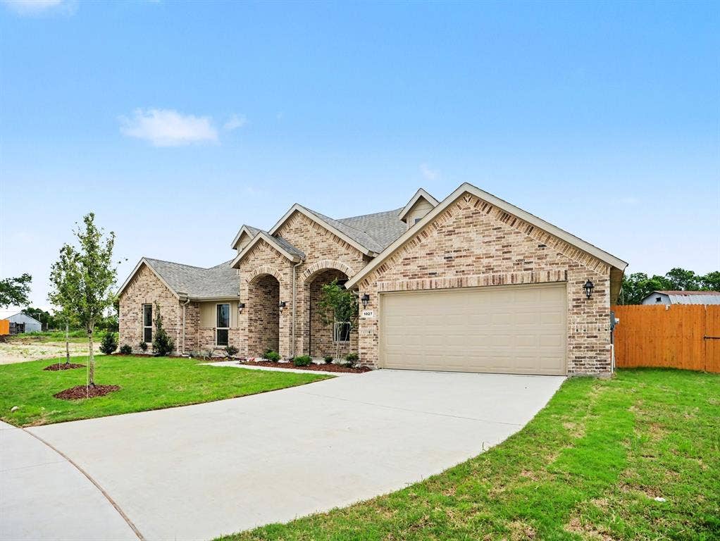 Brick exterior with arched entryways, an attached garage, a concrete driveway, and a fenced yard