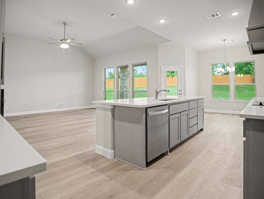 Kitchen island with light grey cabinetry, integrated sink, and stainless steel dishwasher