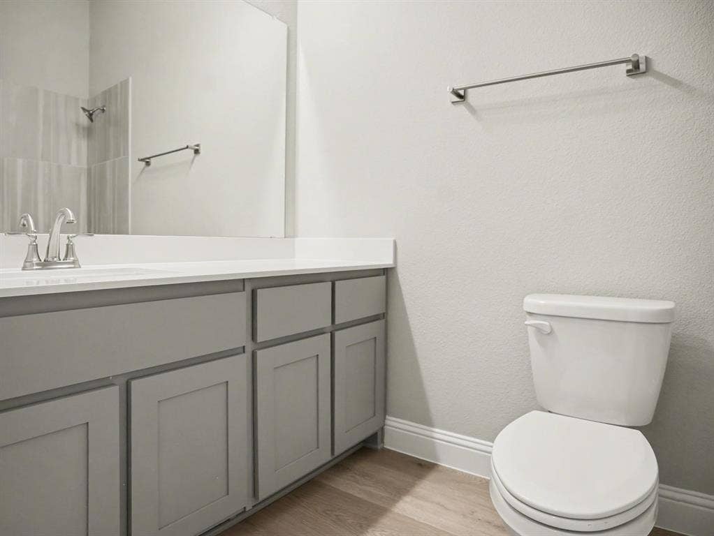 Bathroom featuring a white countertop with an integrated sink, brushed nickel faucet, large vanity mirror, light grey shaker-style cabinetry, and wood-finish flooring