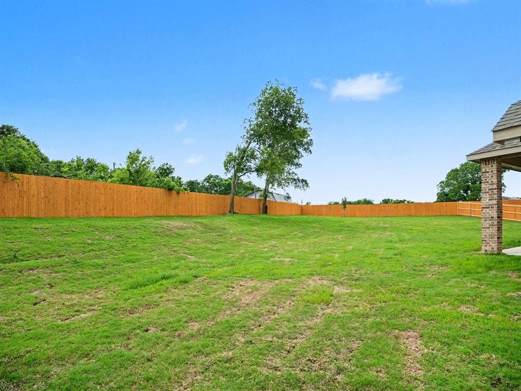 Expansive backyard featuring a lush green lawn, full wood privacy fence, and mature trees