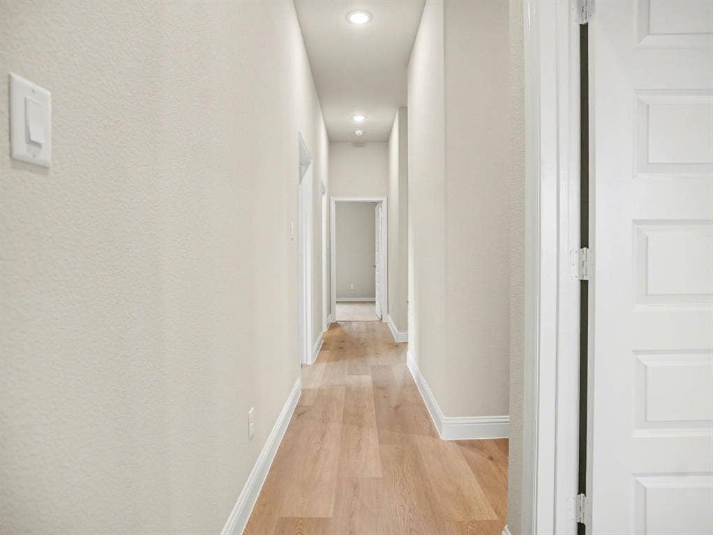 Elongated hallway featuring wood-finish flooring, recessed lighting, neutral wall tones, and white trim