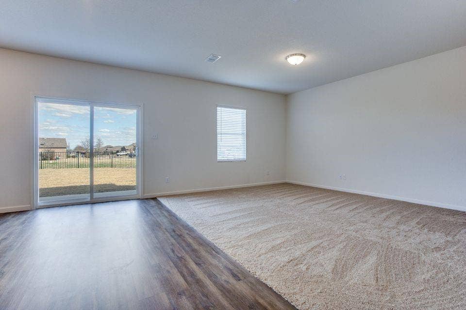 Spacious room featuring a sliding glass door, a single window with blinds, wood-finish flooring, and light-toned carpeting