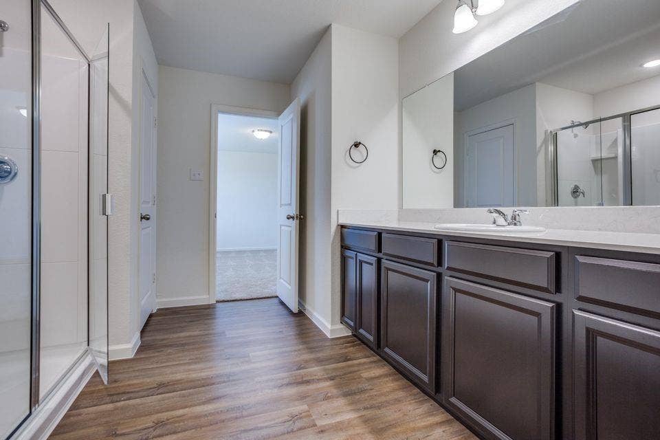 Spacious bathroom featuring wood-finish flooring, a glass-enclosed shower, and a vanity with a light-colored countertop