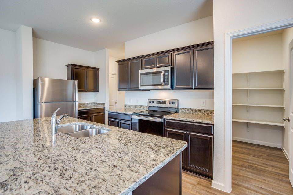 Kitchen featuring an island with a stainless steel double basin sink, dark wood-finish cabinetry, stainless steel appliances, speckled stone countertops, and wood-finish flooring