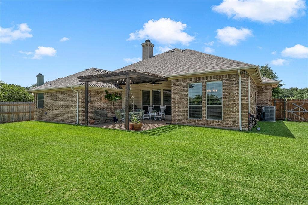 Expansive green lawn bordering a brick exterior with a rear patio featuring a wooden pergola