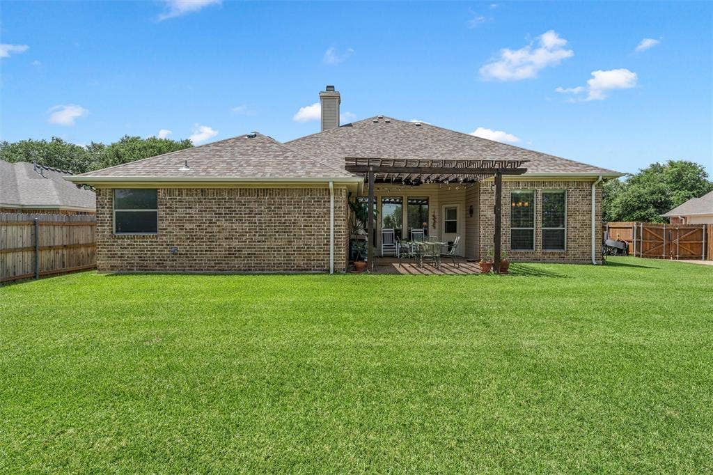 Expansive green lawn with a full brick exterior and a covered patio featuring a wood pergola