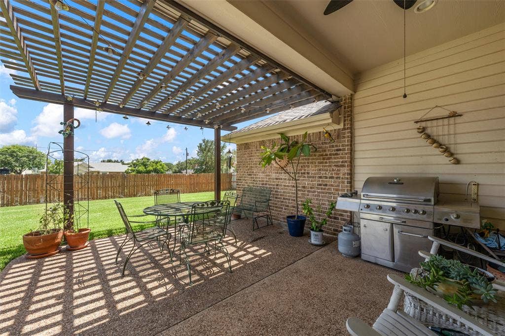 Covered patio area featuring a wooden pergola, an exposed aggregate concrete slab, a ceiling fan, and a brick exterior wall