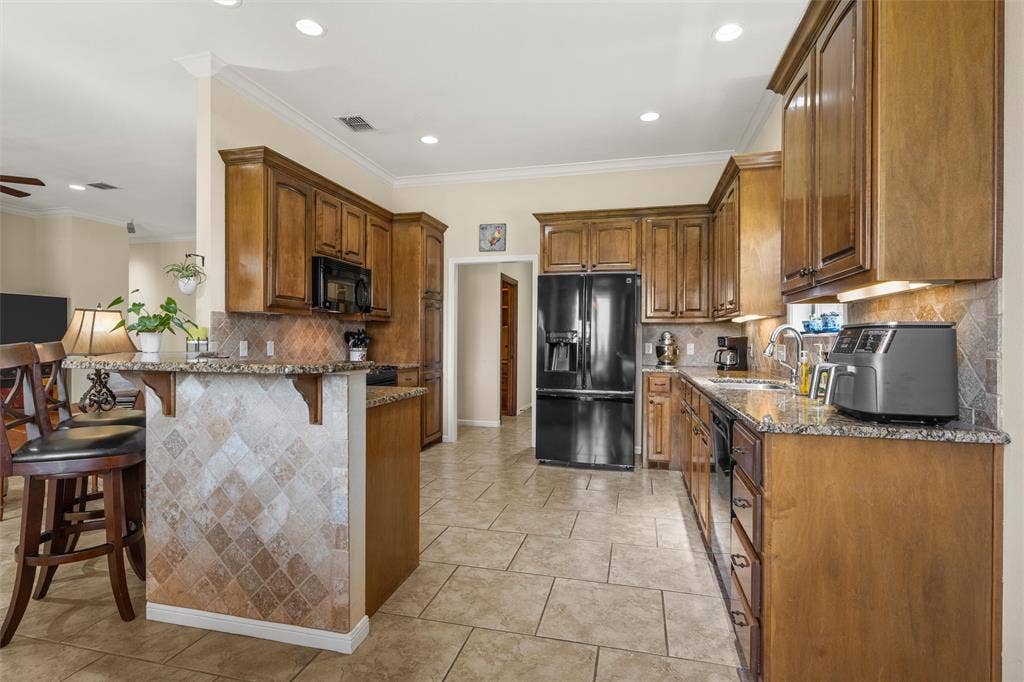 Kitchen featuring wood cabinetry, granite-style countertops, tile flooring, and a breakfast bar with decorative tile accents