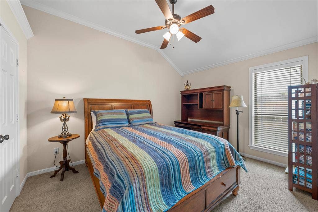 Room featuring a vaulted ceiling with crown molding, a ceiling fan with integrated lighting, and carpet flooring