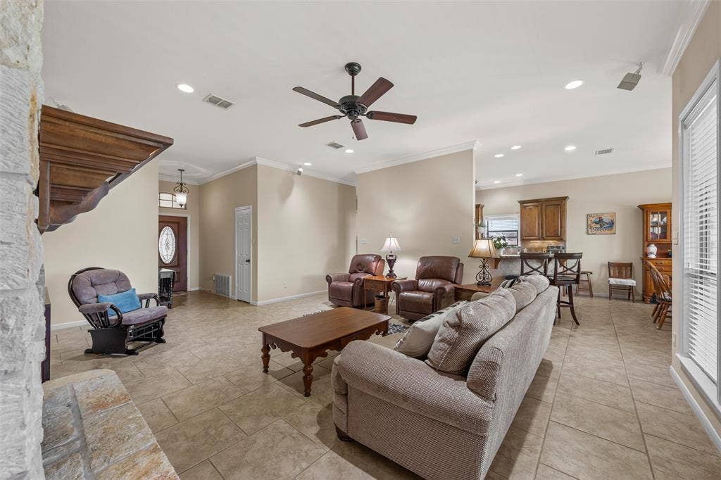 Spacious living area featuring tiled flooring, a stone fireplace surround, and crown molding