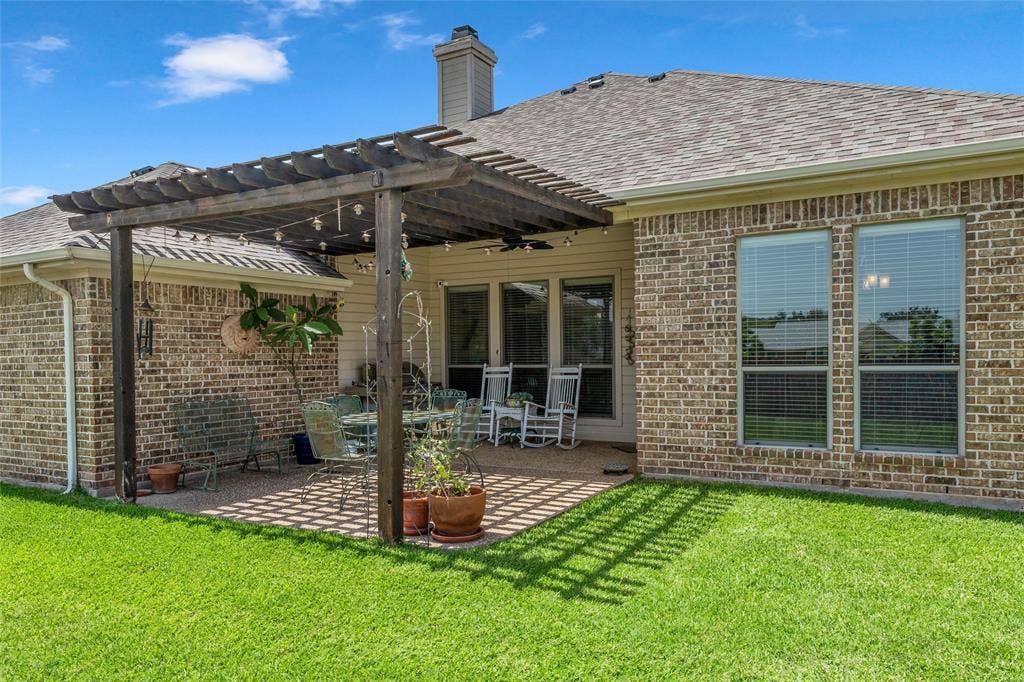 Expansive backyard featuring a pergola-covered patio with string lighting, brick exterior, and a manicured lawn