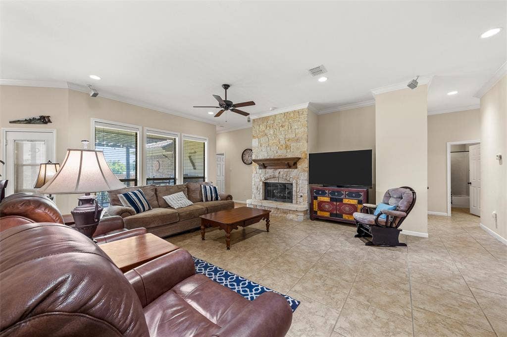 Spacious living area featuring a stone fireplace with a wood mantel, large format tile flooring, crown molding, and recessed lighting