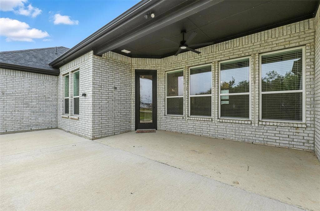 3141 Claire Drive, Midlothian, TX 76065 Expansive concrete patio area with a covered ceiling featuring a ceiling fan, white brick exterior, multiple windows, and a glass-paneled door