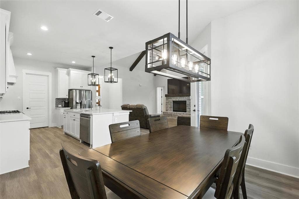 3141 Claire Drive, Midlothian, TX 76065 Open-concept living space featuring wood-finish flooring, a kitchen with white cabinetry and an island, a stainless steel dishwasher, and a living area with a stone-surround fireplace