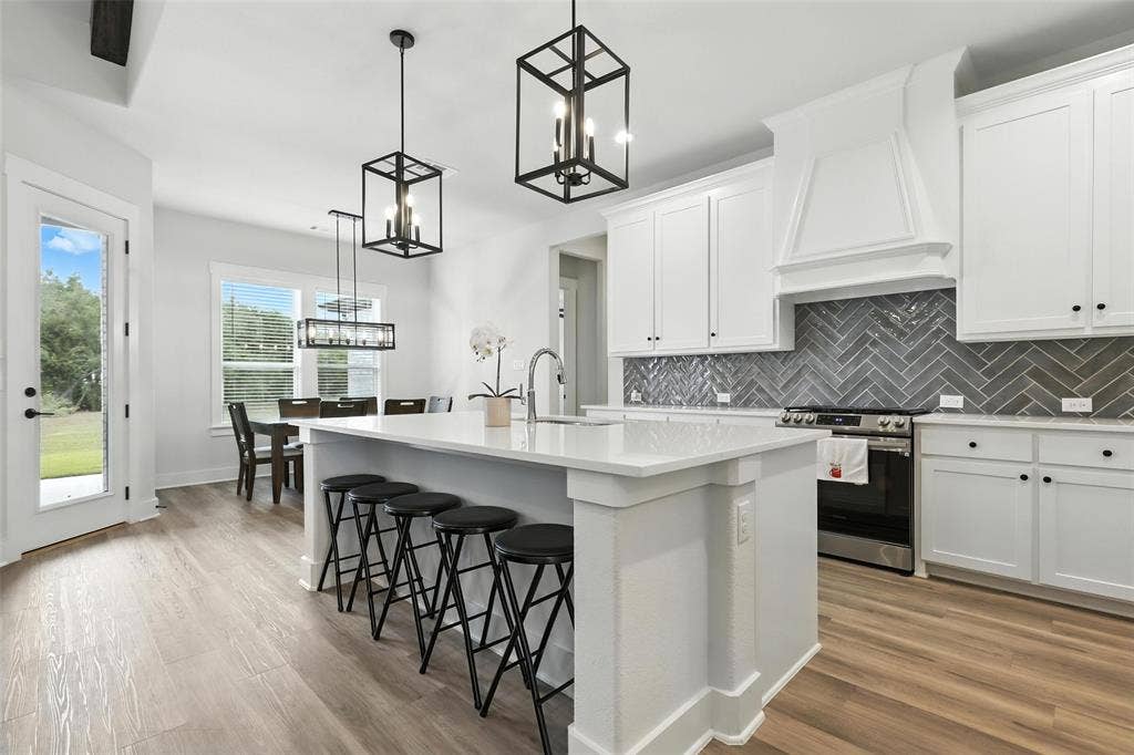 3141 Claire Drive, Midlothian, TX 76065 Modern kitchen featuring a large island with seating, white cabinetry, herringbone tile backsplash, and wood-finish flooring