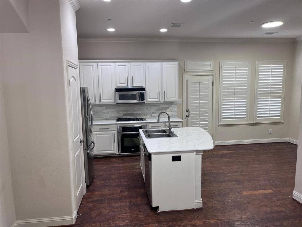 5717 PANTHEON Court, Plano, TX 75024 Modern kitchen featuring white cabinetry, a light-toned tile backsplash, stainless steel appliances, and a central island with an undermount sink