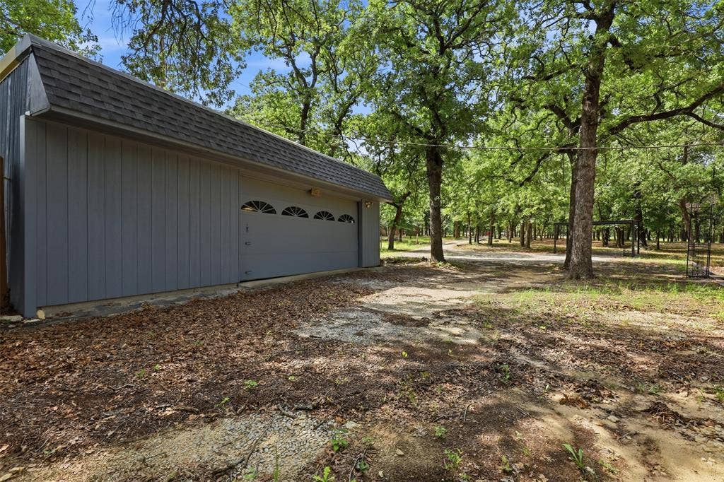 777 Wildwood Trail, Weatherford, TX 76085 Detached garage with panel siding, a shingle roof, and an overhead door featuring arched window inserts