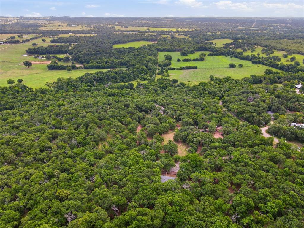 777 Wildwood Trail, Weatherford, TX 76085 Expansive aerial landscape featuring a large wooded area with visible clearings, surrounded by open green fields and additional tree coverage