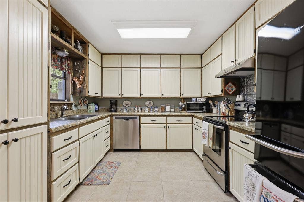 777 Wildwood Trail, Weatherford, TX 76085 U-shaped kitchen featuring cream-colored cabinetry with beadboard paneling, stone-finish countertops, stainless steel appliances, and tile flooring