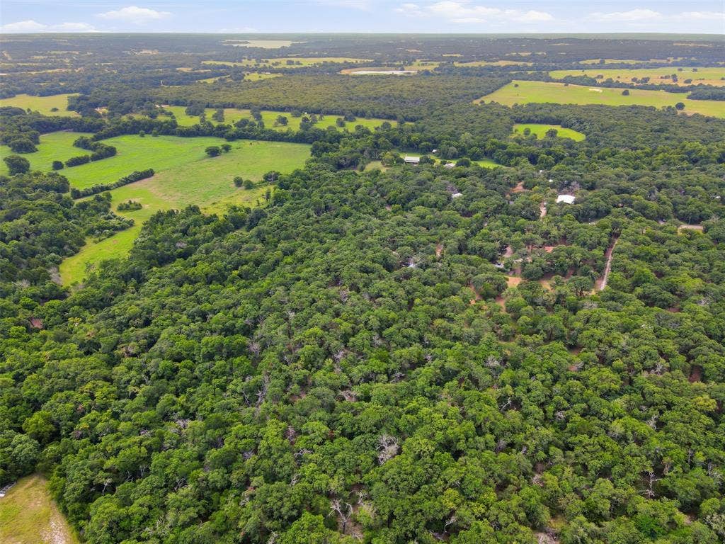 777 Wildwood Trail, Weatherford, TX 76085 Expansive acreage featuring mature tree cover, open green fields, and distant structures under a broad sky